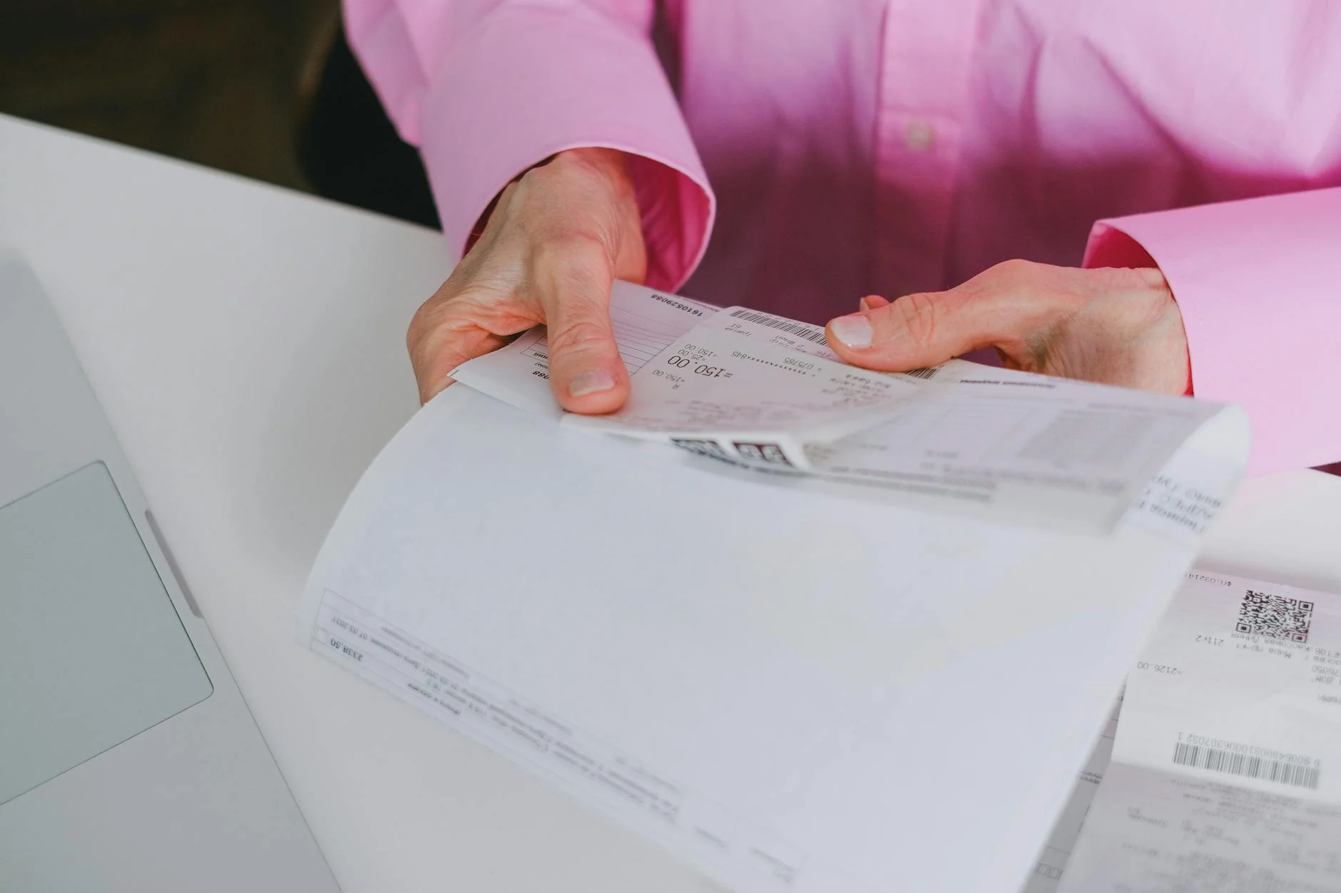 Hands holding printed financial documents on a clean white desk with a laptop in the background
