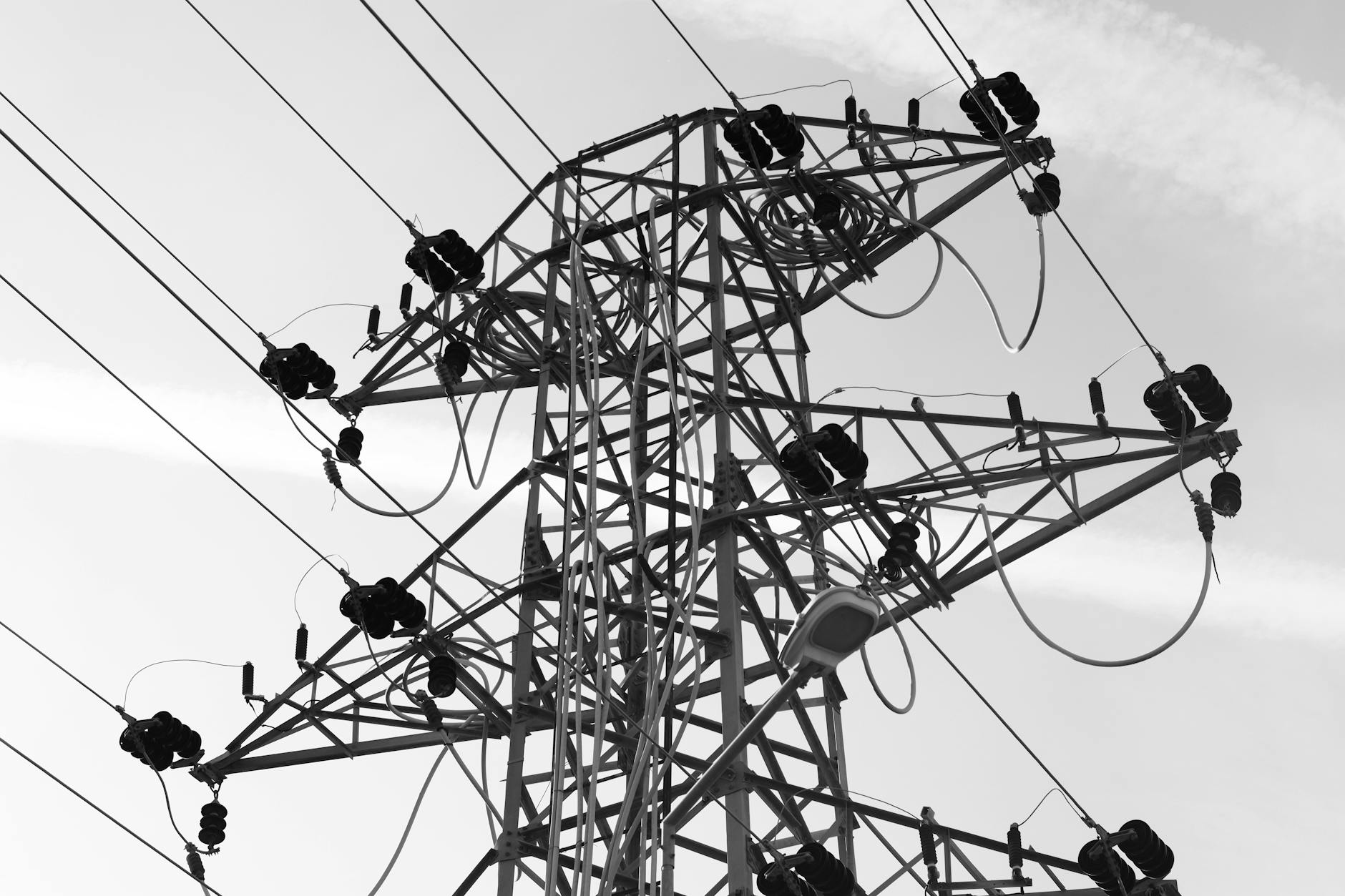 High-voltage electrical transmission tower in black and white against an open sky