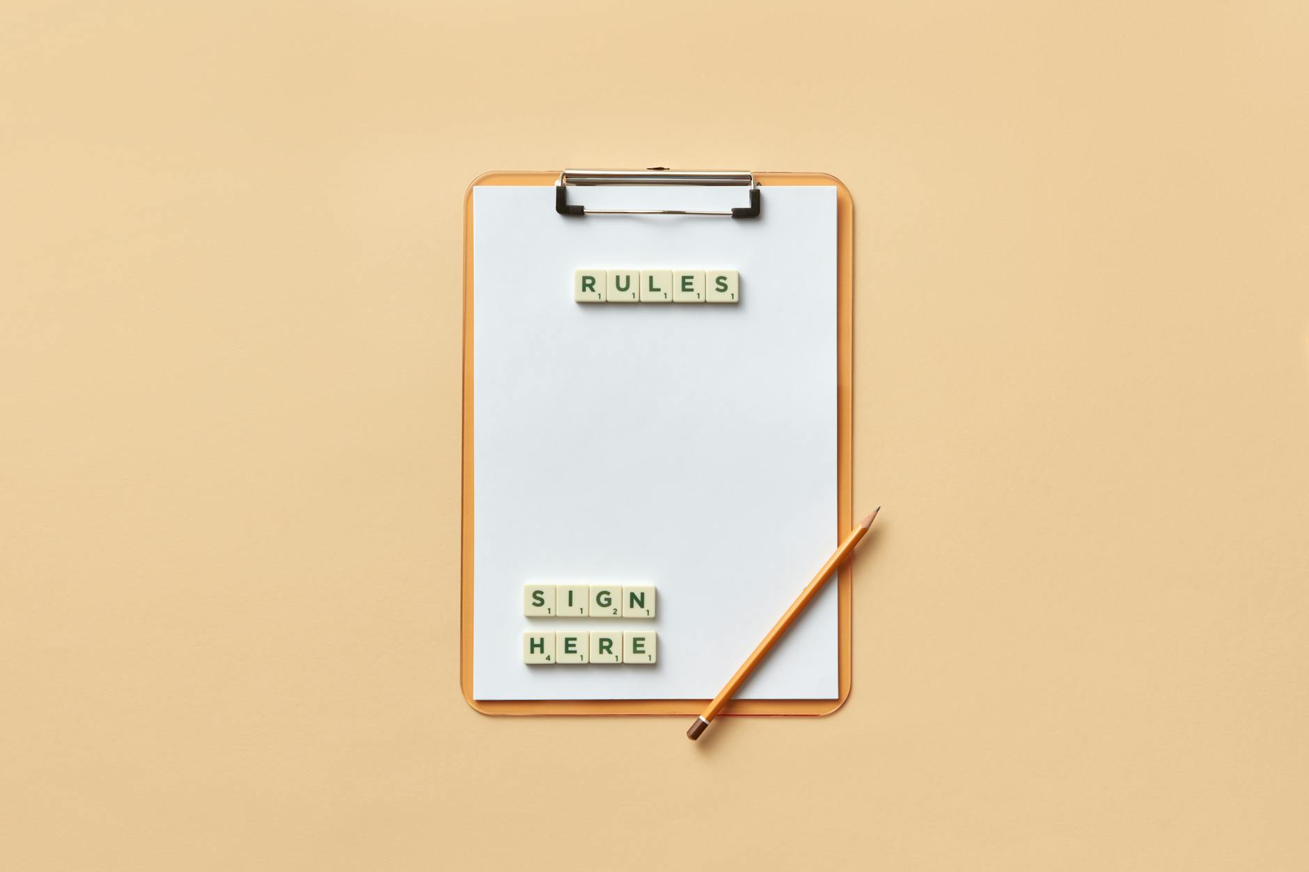 Clipboard with blank paper and letter tiles spelling RULES on a beige background with a pencil